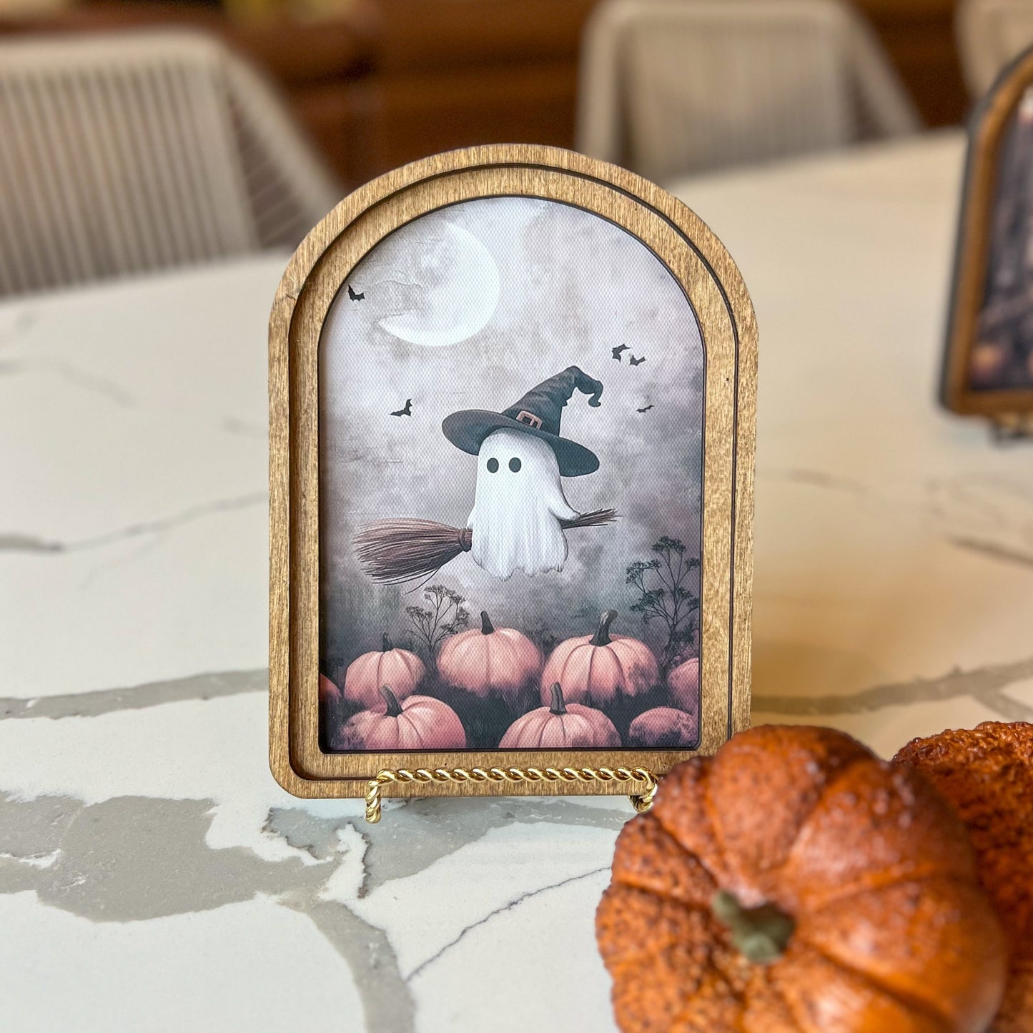 Decorative Halloween sign with ghost and pumpkins on a marble surface.