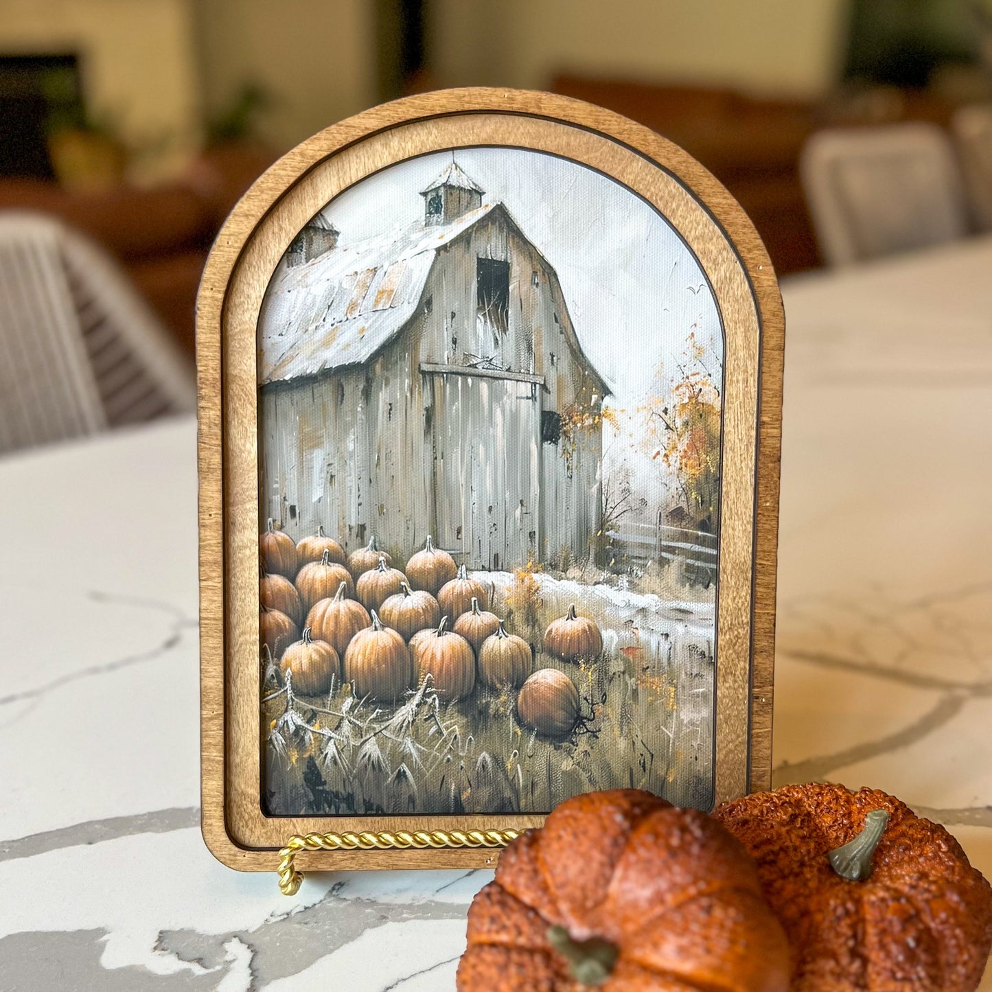 Decorative sign with a barn and pumpkin patch illustration on a marble surface with pumpkins.