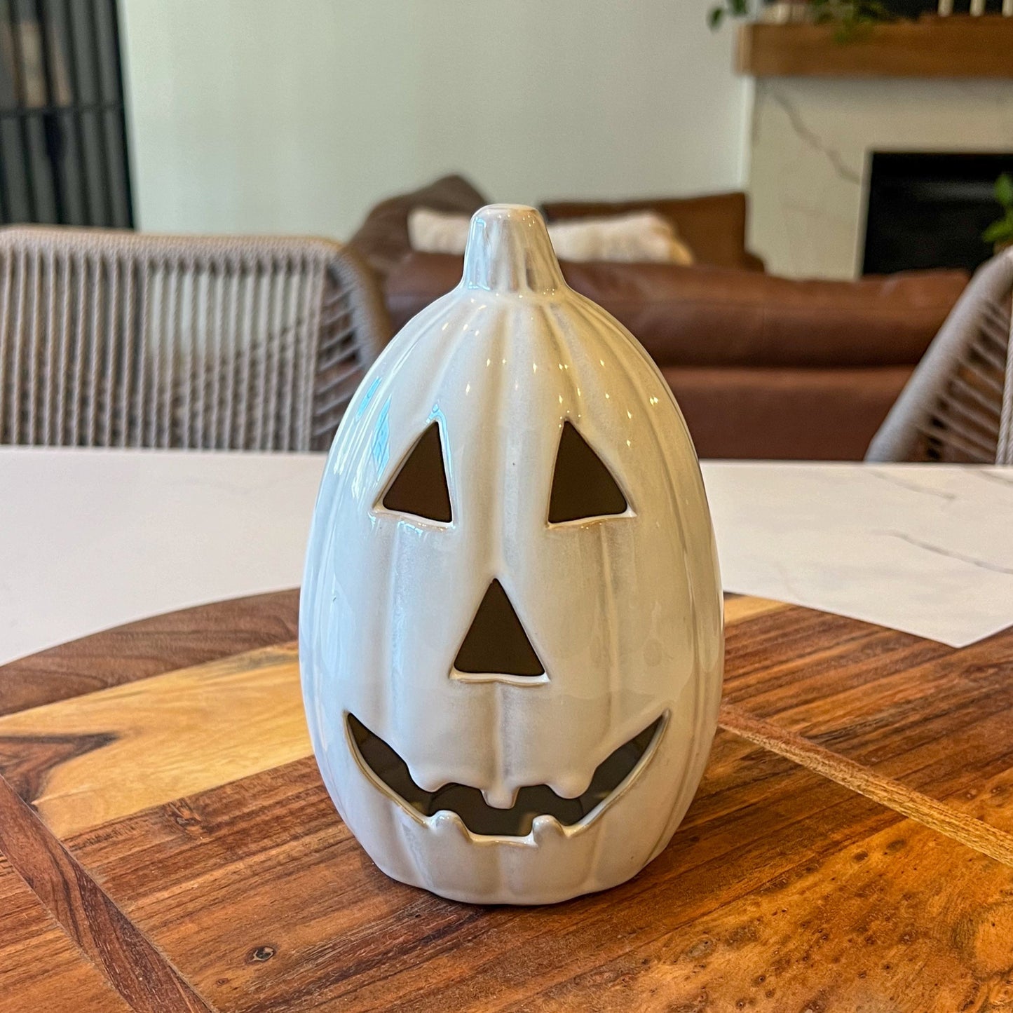 White ceramic jack-o'-lantern on a wooden table with a blurred indoor background