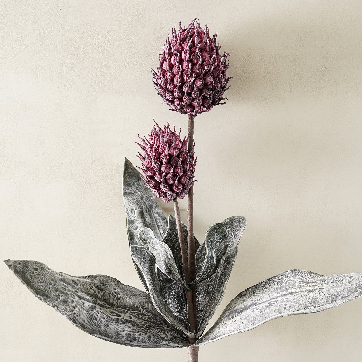 Artificial plant with purple flowers and gray leaves on a beige background