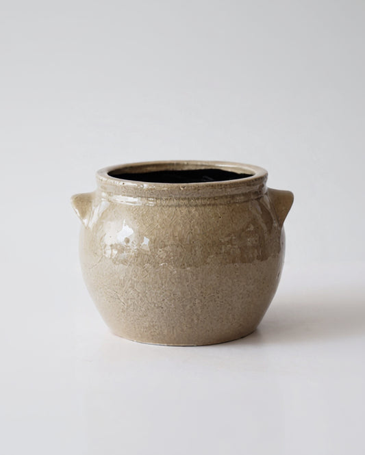 A light beige ceramic crock with handles and a dark beige glaze on the inside.
