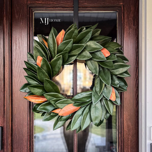 A green and orange magnolia wreath hanging on a brown door