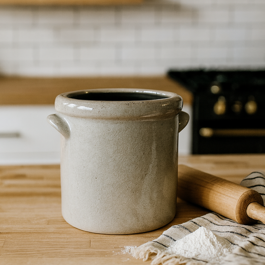 Ceramic pot on a wooden kitchen counter with a rolling pin and towel.