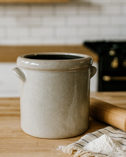 Ceramic pot on a wooden kitchen counter with a rolling pin and towel.