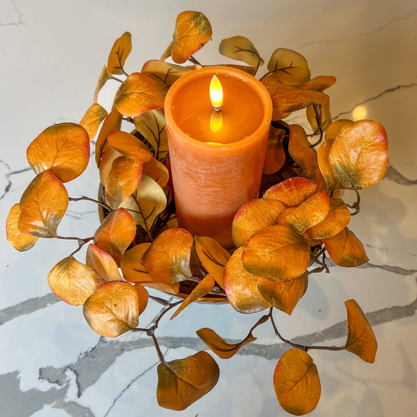 Candle in a decorative holder with orange leaves on a marble surface