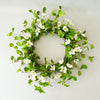 Decorative wreath with green leaves and white flowers on a plain background