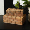 Stack of woven wooden boxes on a dark surface with a vase of white flowers in the background.