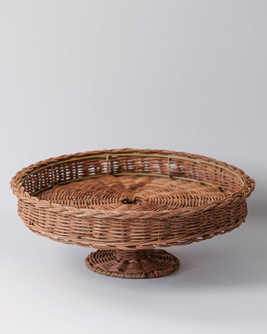 A hand woven rattan pedestal with a round top and a cylindrical base, braided in a natural brown color.