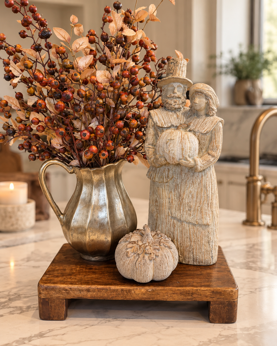 Heirloom Harvest fall styled look featuring antique gold pitcher with autumn berry branches, pilgrim couple, botanical pumpkin and dark wood riser