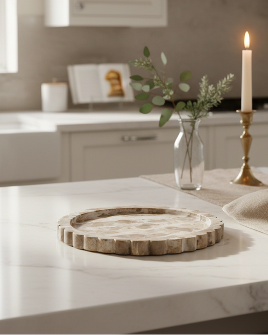 Kitchen counter with a wooden tray, vase with greenery, and lit candles.