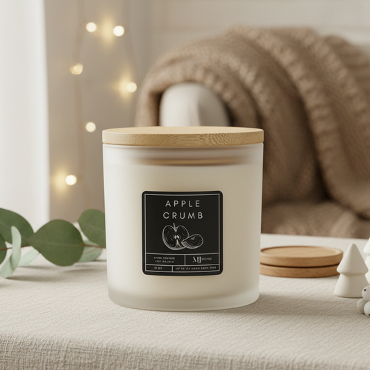 White candle with wooden lid labeled 'Apple Crumb' on a surface with decorative elements.