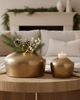 Decorative setup on a wooden coffee table with gold vases, candles, and greenery in a living room.