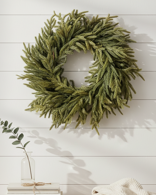 Green wreath on a white wall above a wooden bench with books, a plant, and a blanket.