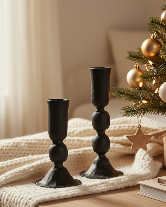 Black candle holders on a table with a Christmas tree in the background