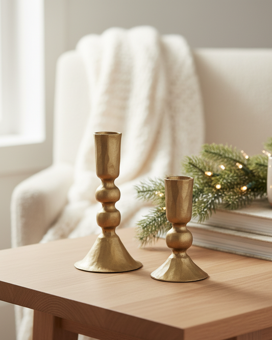 Two gold candle holders on a wooden table with a cozy background