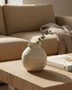Beige textured vase on a wooden coffee table with a beige sofa in the background