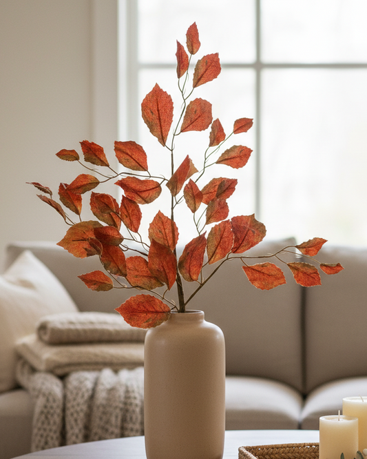 Decorative setup with a vase of red leaves on a coffee table in a living room.
