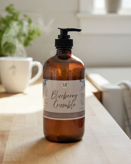 Bottle of 'Blueberry Crumble' soap on a kitchen counter with plants and a bath towel in the background.