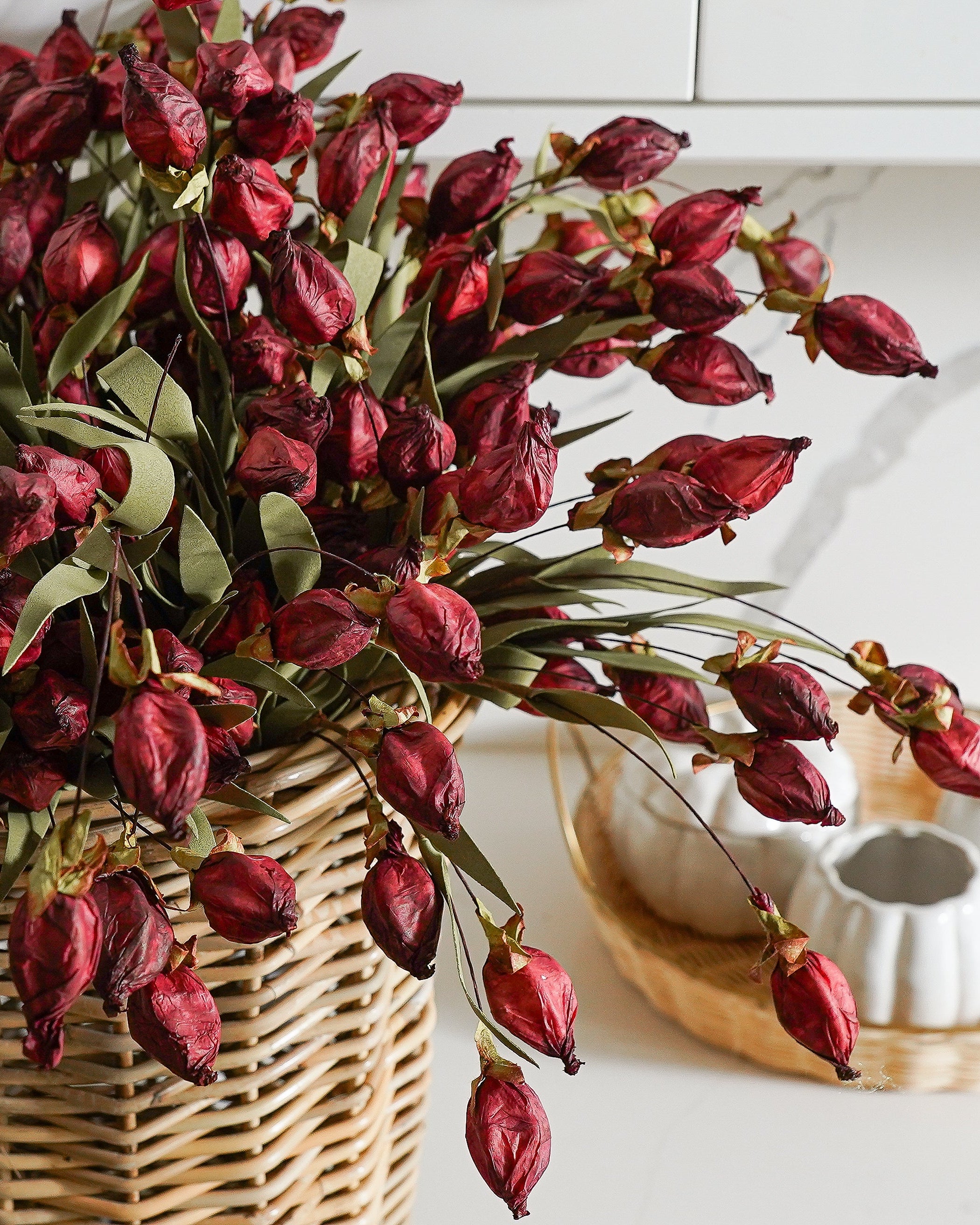 A bouquet of artificial burgundy lantern flowers in a wicker basket, placed on a countertop.