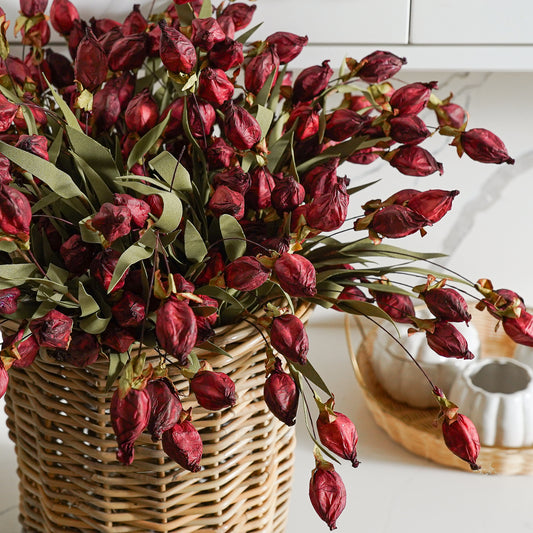 A bouquet of artificial burgundy lantern flowers in a wicker basket, placed on a countertop.