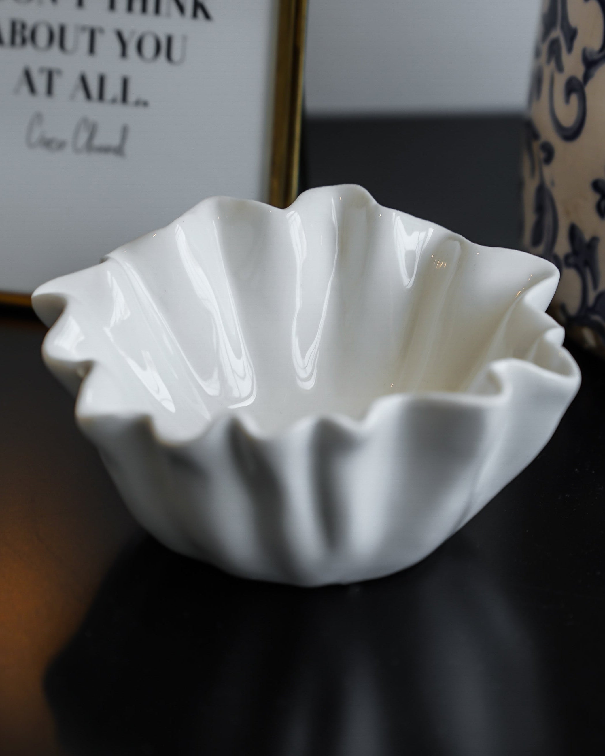 A white stoneware fluted bowl on a dark surface with a patterned wallpaper in the background.