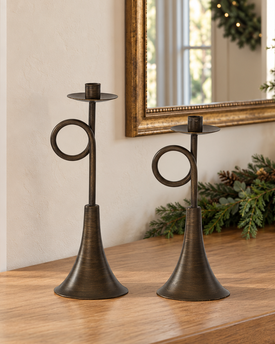 Two bronze iron taper candle holders in coordinating heights with decorative circular loops, slender stems and tapered pedestal bases