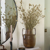 Decorative setup with a vase of dried flowers, books, and a candle on a wooden surface.