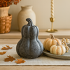 Decorative gourds and pumpkins on a table with autumn leaves and candles in the background.