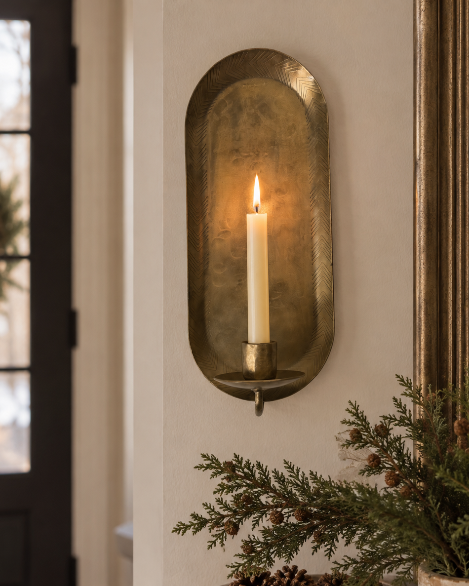 Antique brass iron wall taper candle sconce with elongated rounded backplate and ivory taper candle displayed against a white brick wall