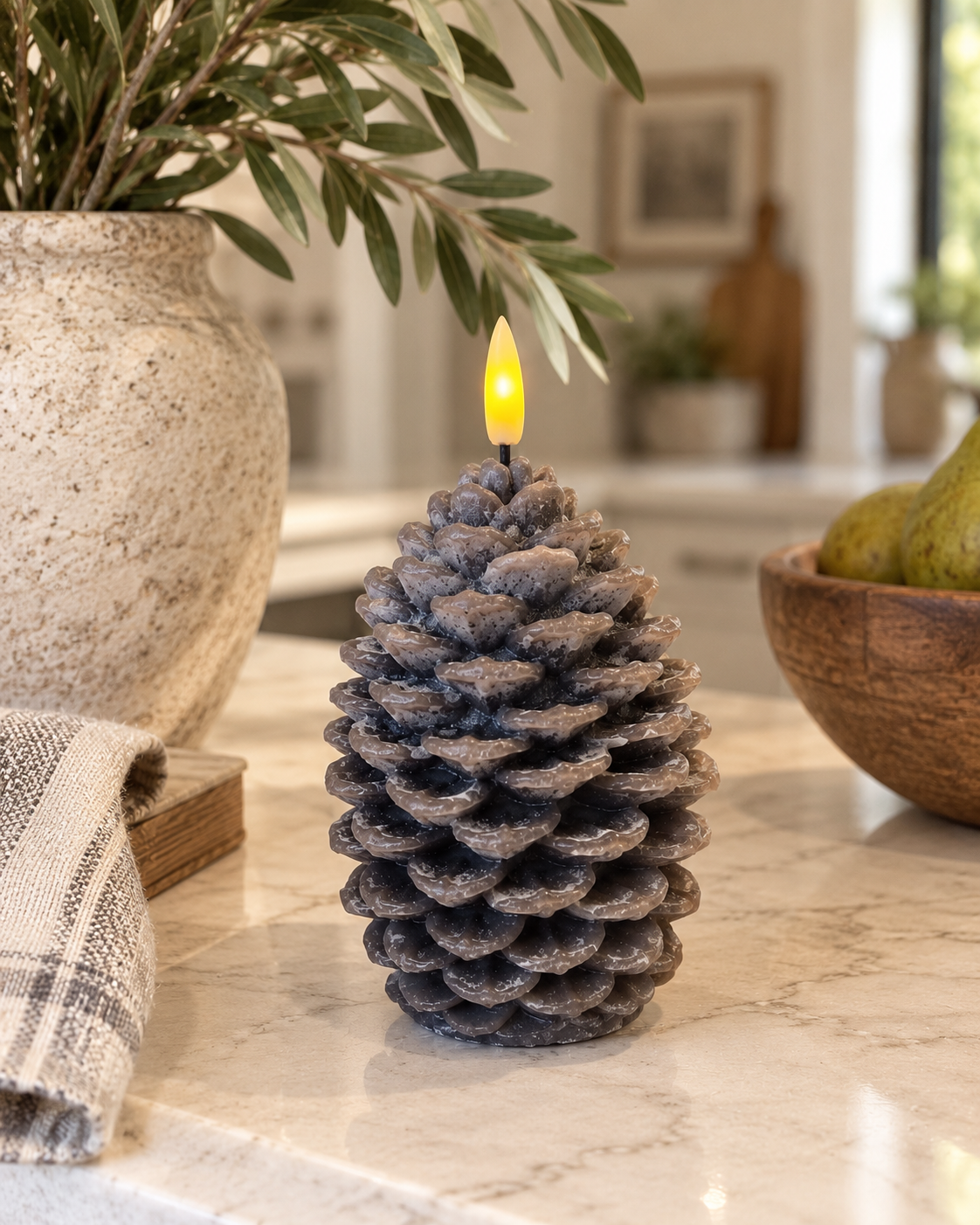 Brown gray flameless LED pinecone candle with realistic layered scales and glowing flame styled on a kitchen countertop