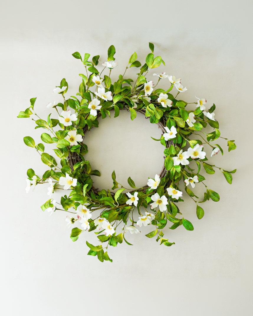 Decorative wreath with green leaves and white flowers on a plain background