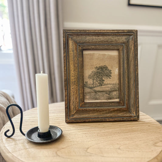 Wooden side table with a framed landscape print and candle