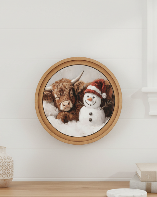 Framed artwork of a cow and snowman on a wall above a wooden surface.