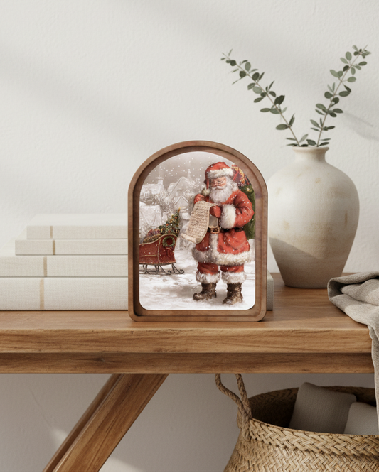 Decorative table with a wooden frame showing a Christmas scene, books, a vase, and a plant.