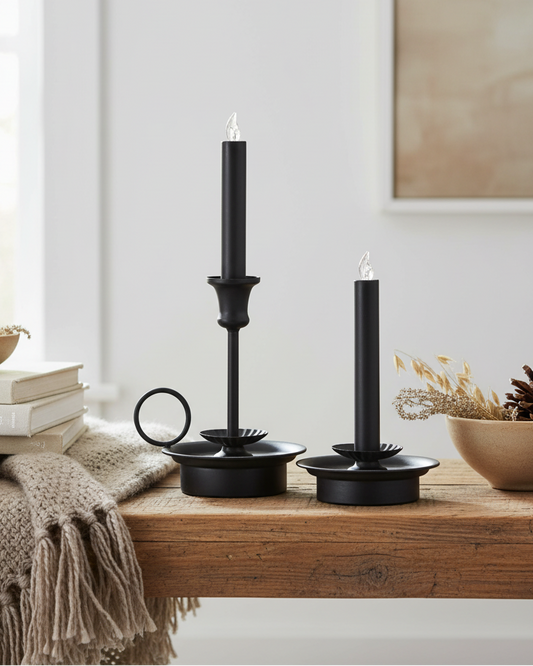 Black candle holders on a wooden surface with books and decorative items in a cozy room.