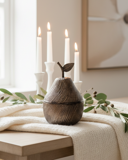 Decorative pear-shaped vase on a table with candles and greenery in a softly lit room.