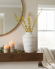 Decorative setup with a vase of yellow flowers, candles, and a blanket on a fireplace mantle.