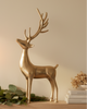 Gold deer ornament on a wooden surface with candles and greenery, in a cozy indoor setting.