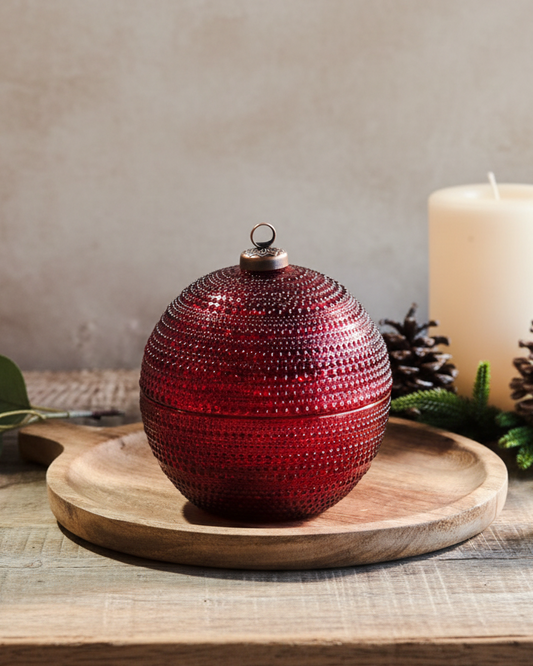 Red textured ornament on a wooden tray with a candle and decorative elements on a neutral background