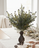 Decorative arrangement of greenery and berries in a vase on a table with a cozy indoor setting.