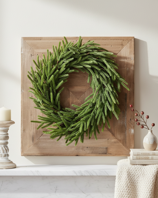 Green wreath on a wooden board against a white wall with decor items.