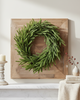 Green wreath on a wooden board against a white wall with decor items.