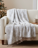 White floral-patterned throw blanket draped over a beige sofa in a cozy living room with a Christmas tree.