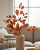 Decorative setup with a vase of red leaves on a coffee table in a living room.